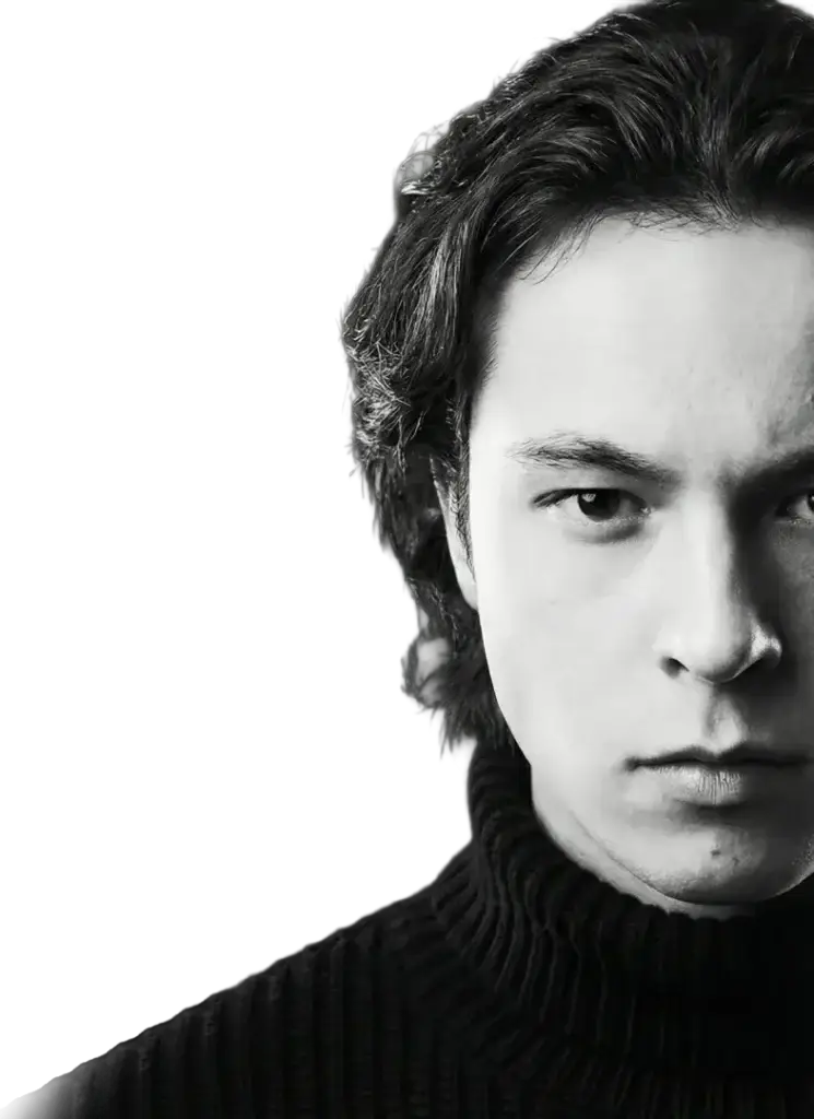 BeWell, real estate ecosystem, designed to elevate human potential Black and white close-up of a young man with long hair, wearing a ribbed turtleneck sweater, staring directly at the camera with a serious expression. Jérémy Savoie